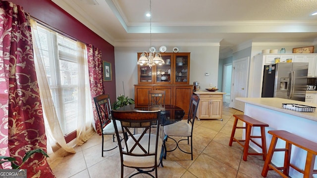 dining space with an inviting chandelier, a tray ceiling, ornamental molding, and light tile patterned flooring