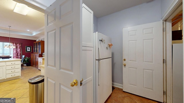 kitchen featuring light tile patterned floors, light countertops, hanging light fixtures, ornamental molding, and freestanding refrigerator