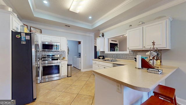 kitchen with a tray ceiling, appliances with stainless steel finishes, washing machine and dryer, white cabinetry, and a sink