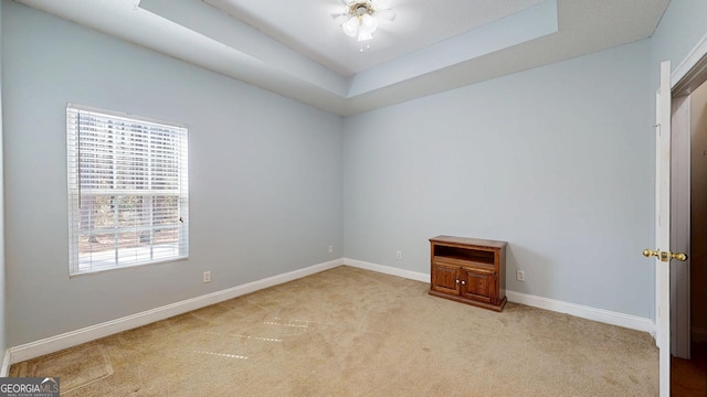 spare room with a raised ceiling, light colored carpet, and baseboards