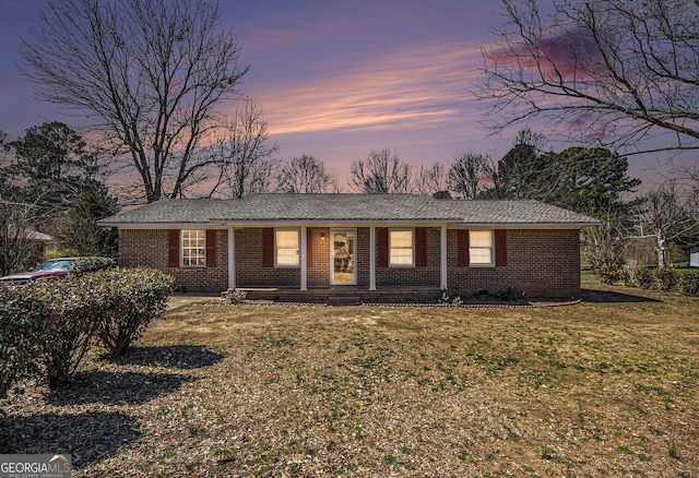 single story home featuring a porch, a lawn, and brick siding