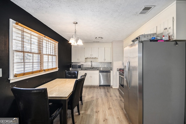 kitchen with visible vents, stainless steel appliances, light wood-style floors, white cabinetry, and a sink