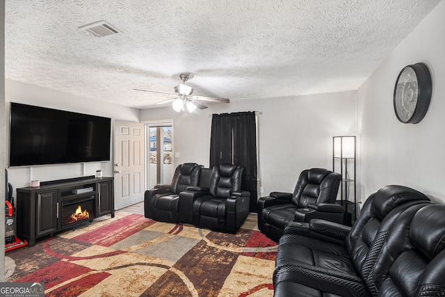 living area with visible vents, ceiling fan, a lit fireplace, a textured ceiling, and light wood-type flooring