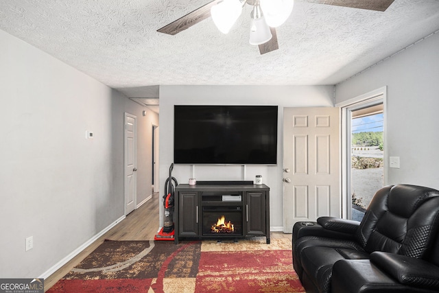 living area with baseboards, a lit fireplace, wood finished floors, a textured ceiling, and a ceiling fan