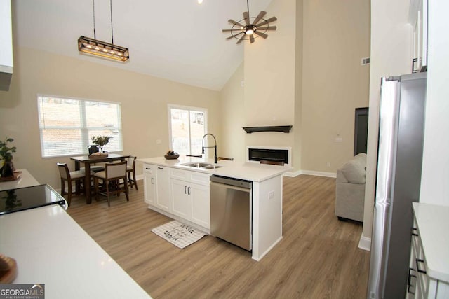 kitchen with a sink, white cabinets, open floor plan, appliances with stainless steel finishes, and a glass covered fireplace