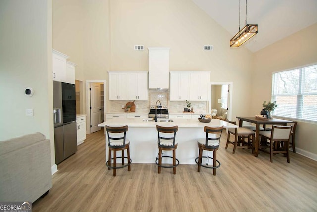 kitchen with custom exhaust hood, a breakfast bar area, light countertops, visible vents, and white cabinetry