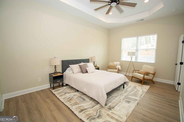 bedroom featuring a raised ceiling, visible vents, baseboards, and wood finished floors