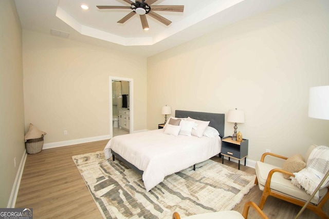 bedroom featuring connected bathroom, recessed lighting, baseboards, light wood-type flooring, and a tray ceiling