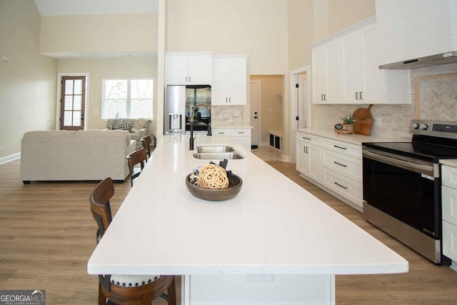 kitchen featuring a breakfast bar, a sink, white cabinets, appliances with stainless steel finishes, and a large island with sink