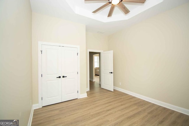 unfurnished bedroom featuring a closet, a raised ceiling, light wood-style flooring, a ceiling fan, and baseboards