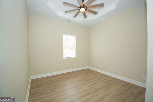 spare room with ceiling fan, wood finished floors, visible vents, baseboards, and a tray ceiling