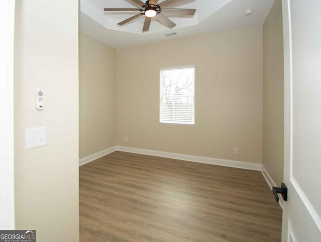 empty room with a ceiling fan, wood finished floors, visible vents, and baseboards