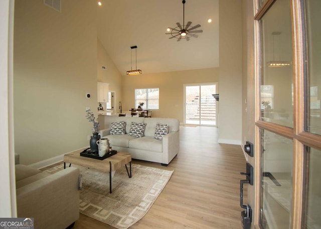 living room with baseboards, visible vents, a ceiling fan, light wood-type flooring, and high vaulted ceiling