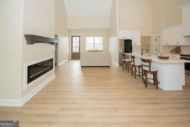 living room with baseboards, a glass covered fireplace, a towering ceiling, and light wood-style floors