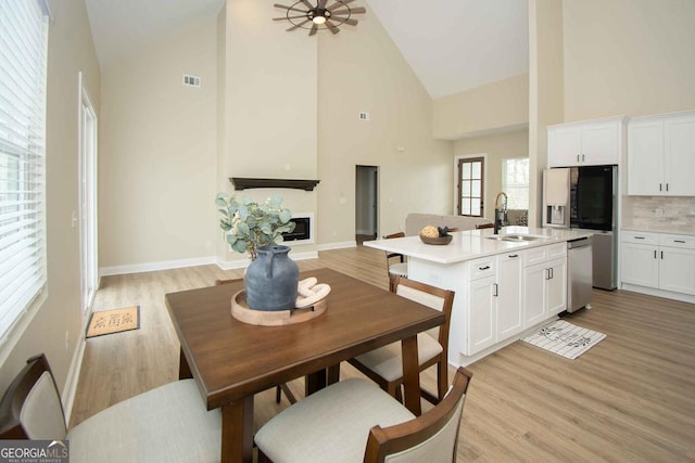 dining room featuring light wood-type flooring, high vaulted ceiling, a fireplace, and visible vents