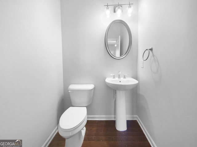 half bath with toilet, a sink, baseboards, and wood finished floors