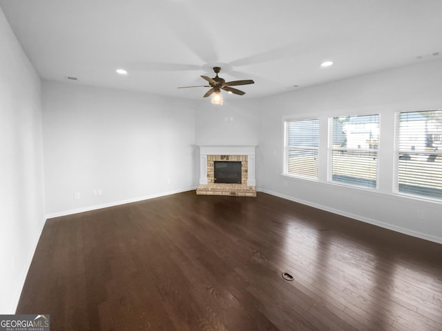 unfurnished living room with a brick fireplace, dark wood finished floors, a wealth of natural light, and baseboards