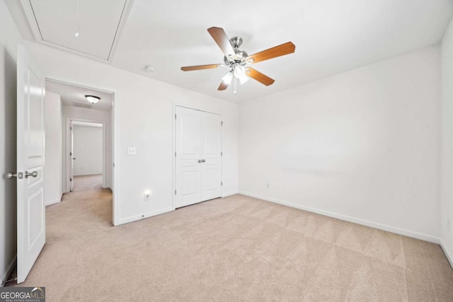 unfurnished bedroom with a closet, light colored carpet, attic access, a ceiling fan, and baseboards