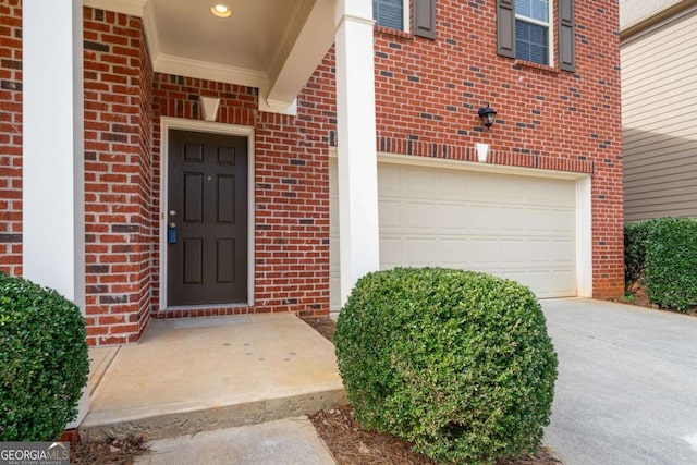 doorway to property with a garage, concrete driveway, and brick siding