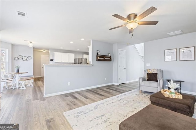 living room with visible vents, baseboards, light wood-type flooring, and ceiling fan