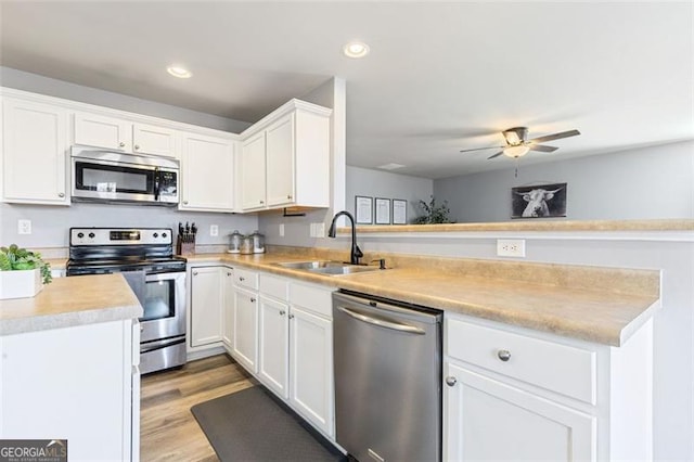 kitchen with a sink, appliances with stainless steel finishes, a peninsula, light wood finished floors, and light countertops