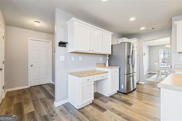 kitchen featuring stainless steel refrigerator with ice dispenser, wood finished floors, white cabinetry, light countertops, and baseboards