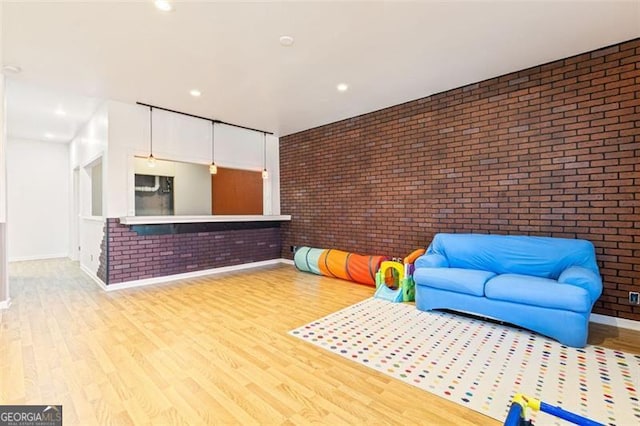 rec room featuring recessed lighting, wood finished floors, baseboards, and brick wall