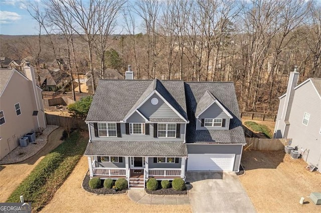 traditional home featuring driveway, a porch, fence, a shingled roof, and a garage