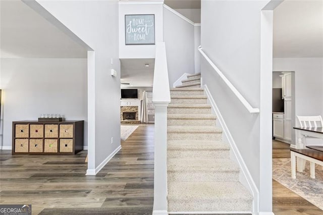 stairs with a fireplace with raised hearth, baseboards, and wood finished floors