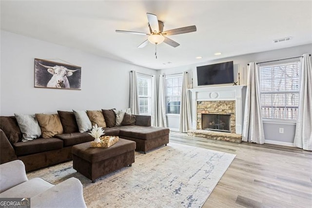 living room with visible vents, wood finished floors, a stone fireplace, baseboards, and ceiling fan