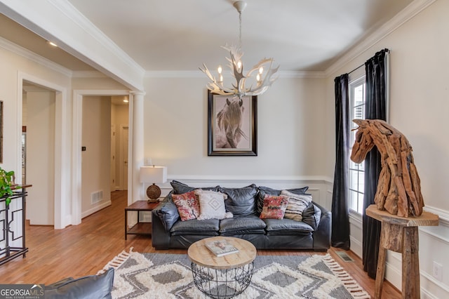 living area with an inviting chandelier, wood finished floors, decorative columns, and crown molding