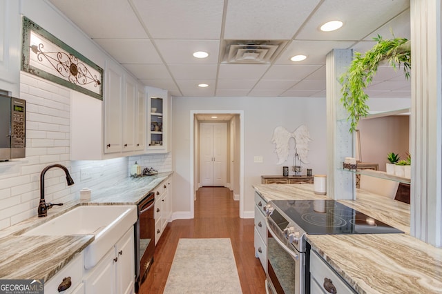 kitchen featuring stainless steel appliances, backsplash, white cabinetry, a sink, and wood finished floors