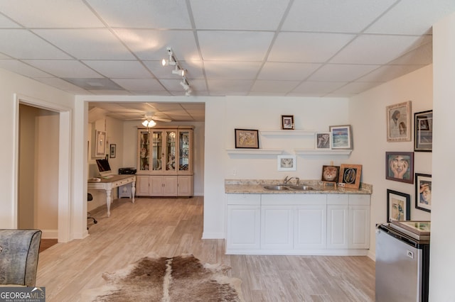 kitchen featuring stove, white cabinets, a sink, light wood-type flooring, and a drop ceiling