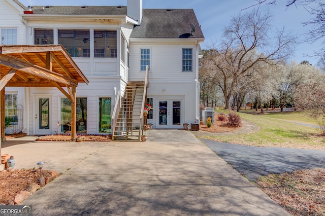 back of house with french doors, a chimney, a shingled roof, stairway, and central AC unit