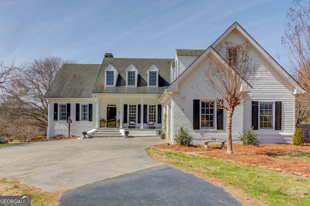 cape cod house featuring a shingled roof, driveway, and a porch