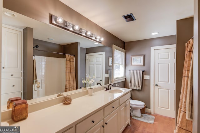 bathroom with toilet, wood finished floors, visible vents, vanity, and baseboards