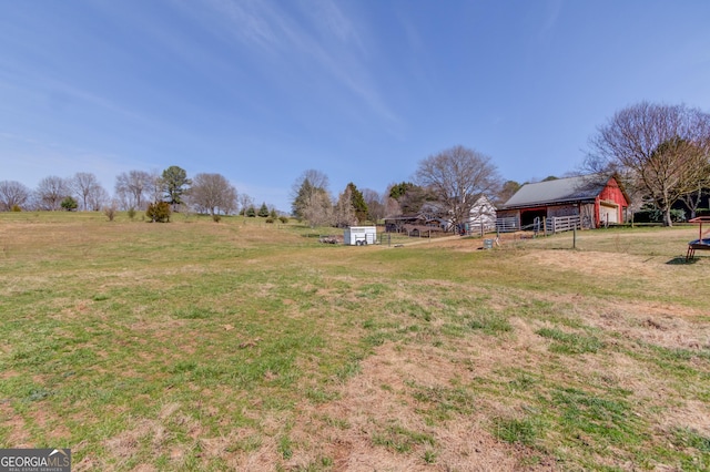 view of yard with a detached garage, a rural view, an outbuilding, fence, and an outdoor structure