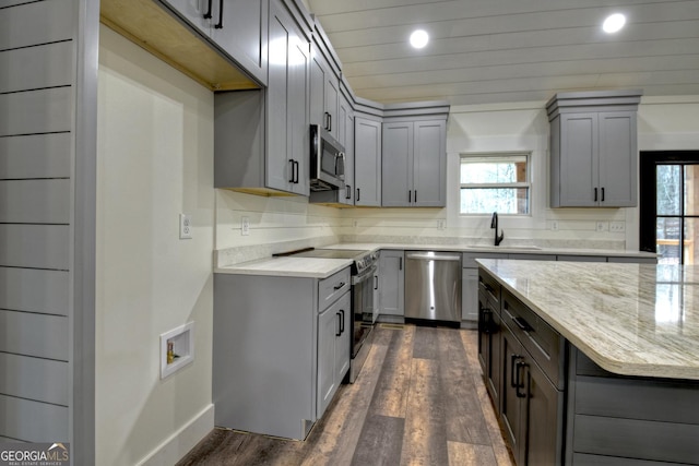 kitchen featuring appliances with stainless steel finishes, dark wood-type flooring, light stone countertops, gray cabinets, and a sink