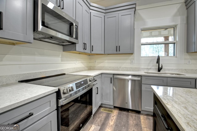 kitchen featuring dark wood-style floors, stainless steel appliances, gray cabinetry, a sink, and light stone countertops