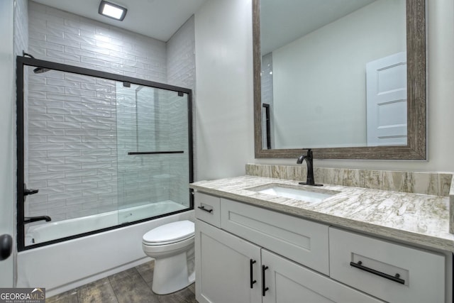 bathroom featuring enclosed tub / shower combo, vanity, toilet, and wood finished floors