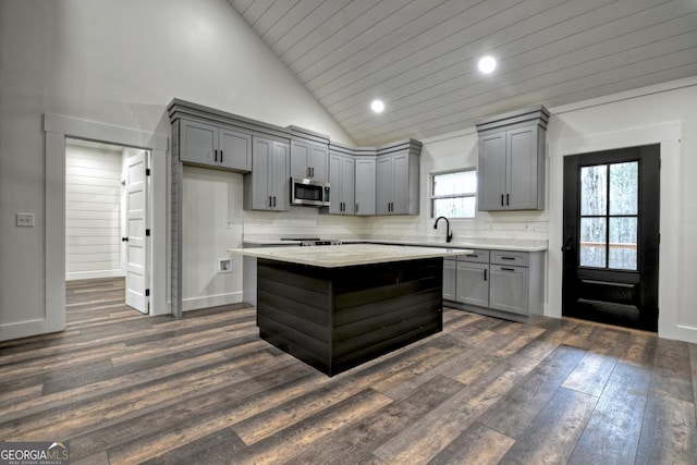 kitchen featuring a center island, stainless steel microwave, backsplash, gray cabinetry, and dark wood-type flooring