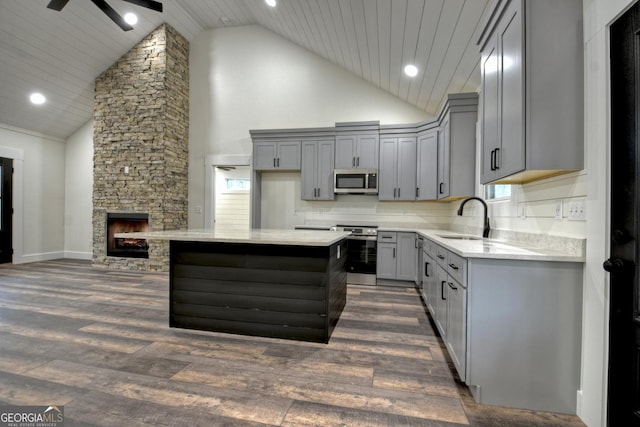 kitchen featuring dark wood-style floors, gray cabinetry, appliances with stainless steel finishes, a stone fireplace, and a sink