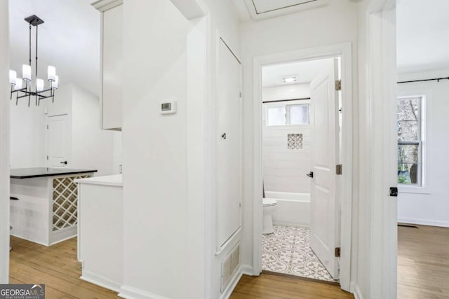 hall with baseboards, light wood finished floors, visible vents, and a notable chandelier