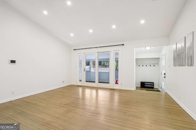 unfurnished living room with lofted ceiling, light wood finished floors, and baseboards