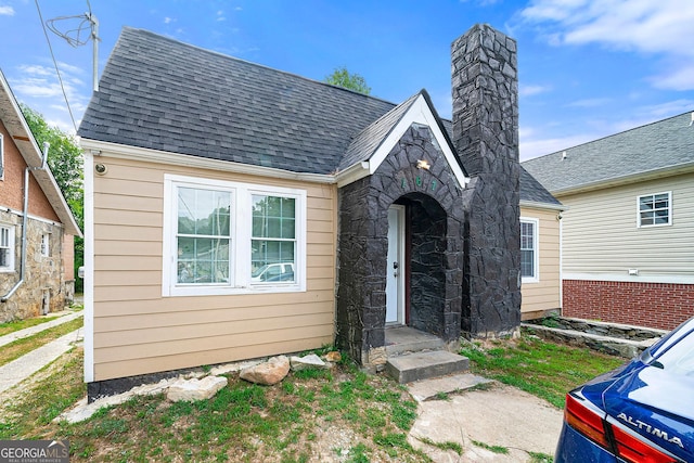 view of front of house featuring stone siding, roof with shingles, and a chimney