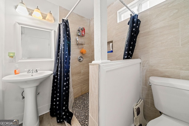 full bathroom featuring toilet, a sink, a tile shower, and tile walls