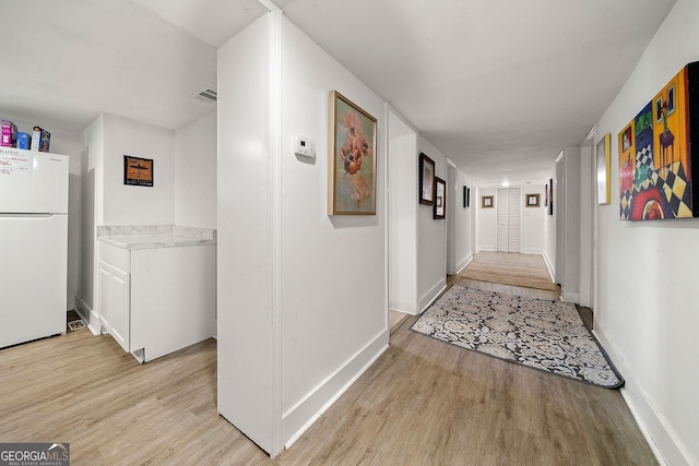 hall featuring light wood-type flooring, visible vents, and baseboards