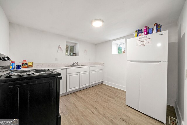 kitchen featuring black range with electric cooktop, a sink, white cabinetry, light countertops, and freestanding refrigerator