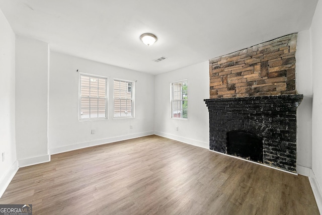 unfurnished living room with a fireplace, wood finished floors, visible vents, and baseboards