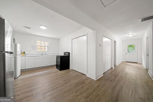 kitchen featuring visible vents, black electric range, freestanding refrigerator, and light wood-style floors